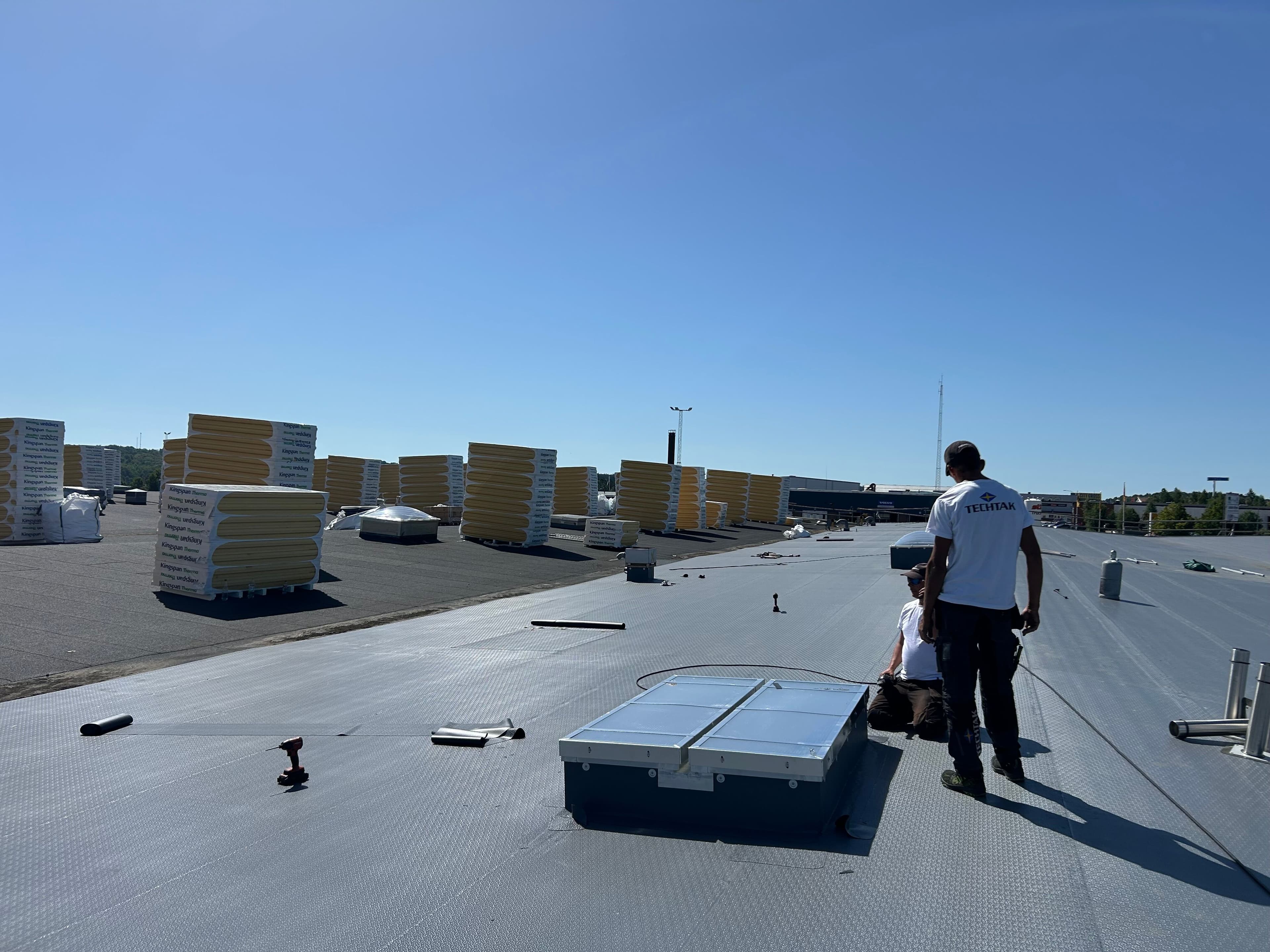 Takläggare installerar ett takfönster på ett platt tak under en takrenovering med Kingspan Therma isolerskivor. Staplade isolerskivor syns på taket under pågående arbete.