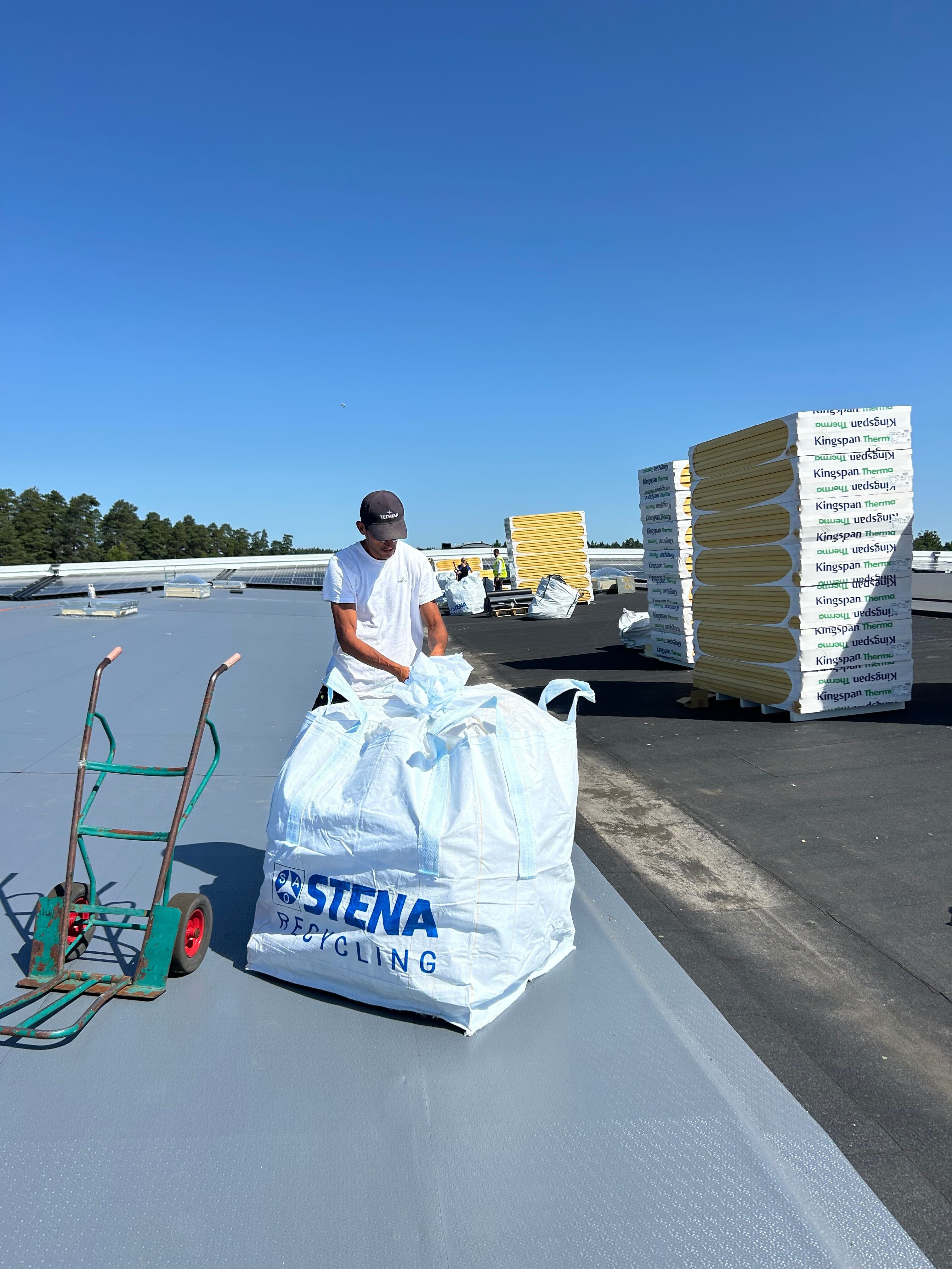 Takläggare samlar in spill från Kingspan Therma isolerskivor i en återvinningssäck från Stena Recycling under en takrenovering.
