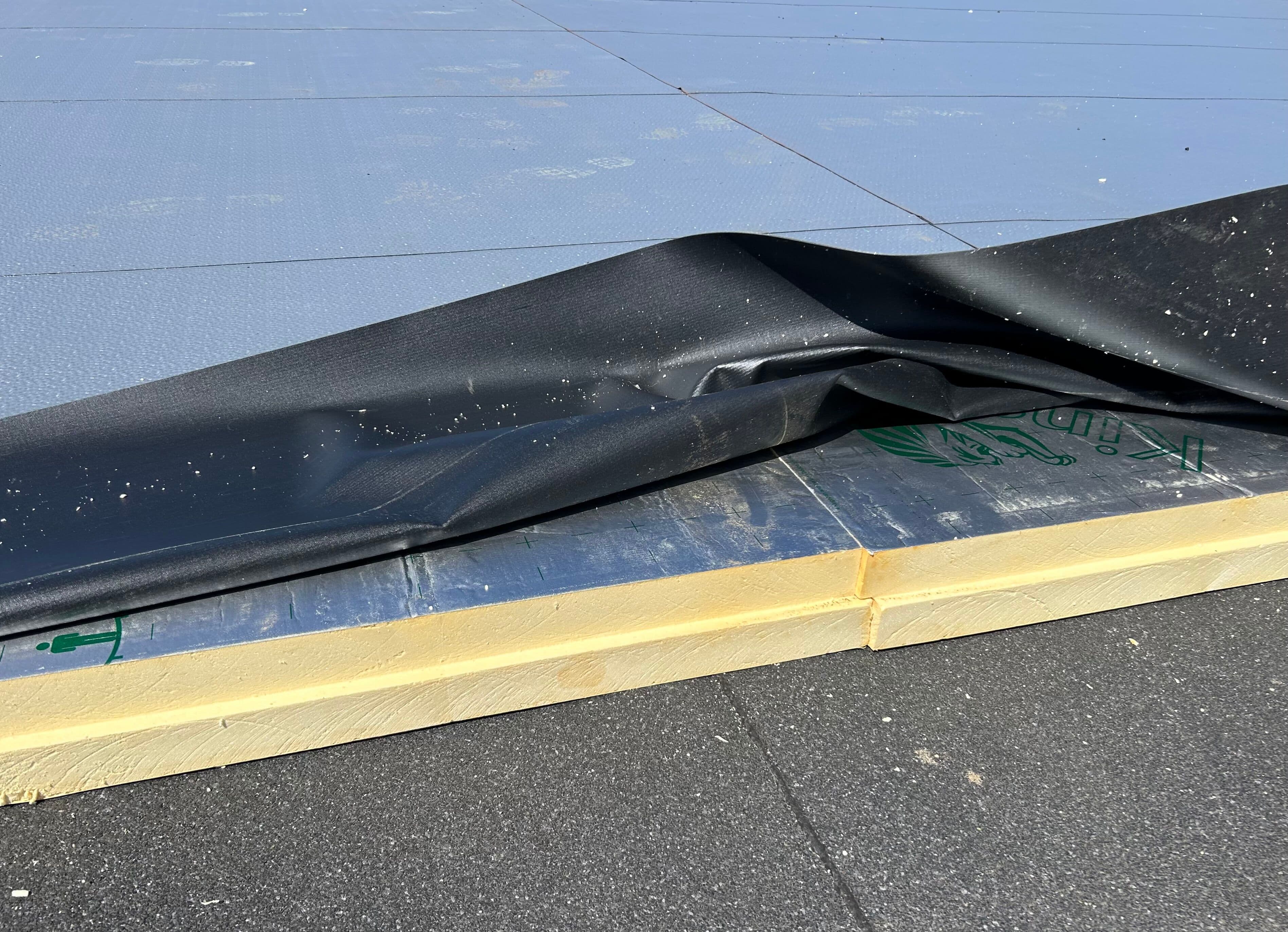 Närbild av Kingspan Therma isolerskivor på ett platt tak under installation. Takduken är uppvikt för att visa isoleringen innan den färdiga taktäckningen monteras.