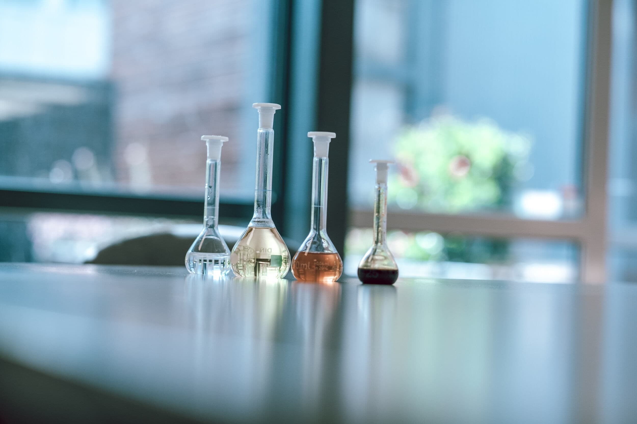 Laboratoriumkolven met heldere, amberkleurige en donkere vloeistoffen op een werkblad, die verschillende fasen van de verwerking van biobased materialen laten zien.